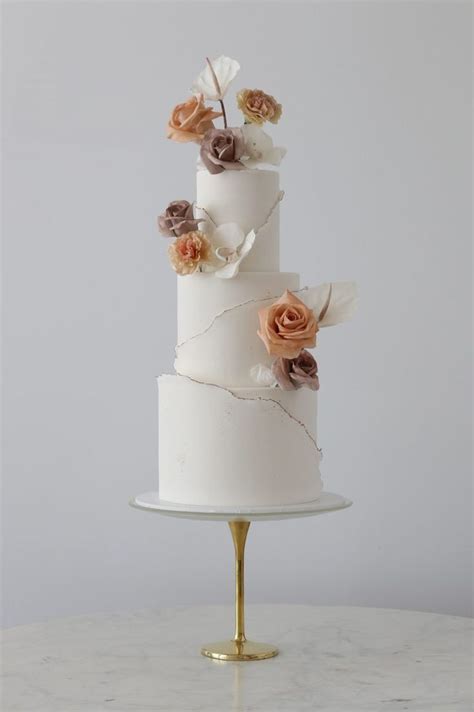 a three tiered wedding cake with flowers on top is sitting on a marble table