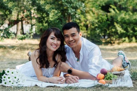 Smiling Asian Couple Happing Picnic In A Park Lying On Their Stomachs
