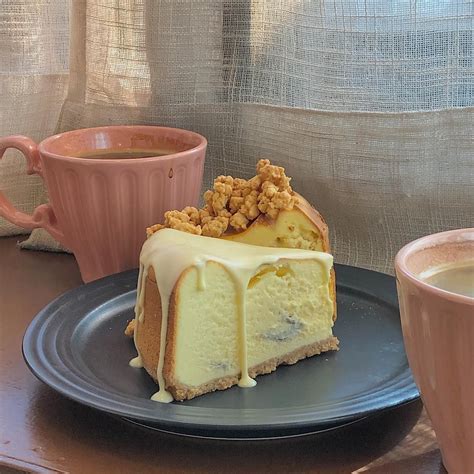 A Piece Of Cheesecake On A Plate Next To Two Cups Of Coffee