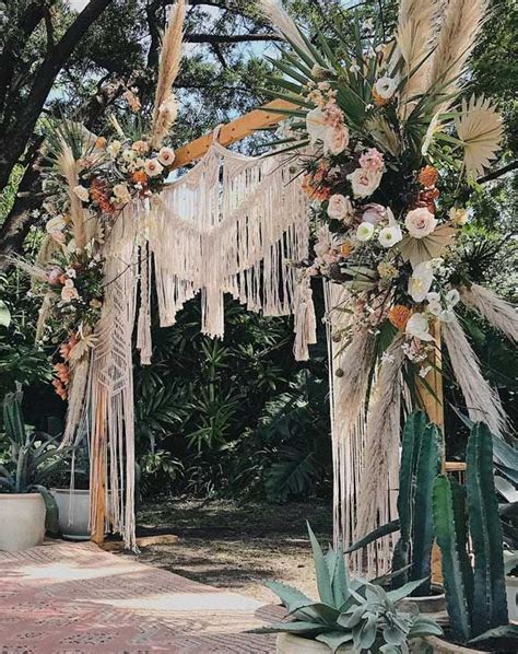 An Outdoor Wedding Arch Decorated With Flowers And Fringes Surrounded