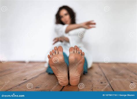 women`s bare feet in the foreground the girl is sitting on a wooden floor on a white background