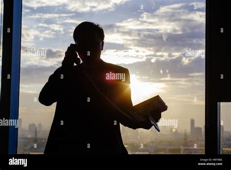 Silhouette Of A Businessman Holding Telephone In Fron Of The Window In