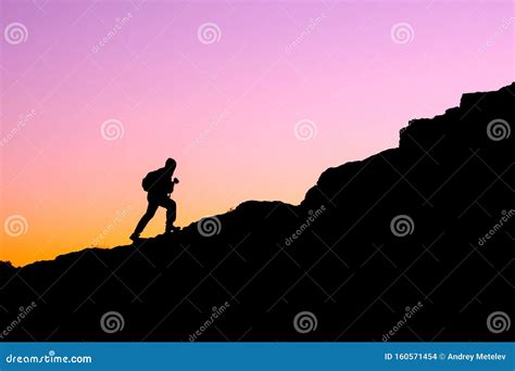 The Silhouette Of A Man Climbing A Mountain In The Sunset Light Stock