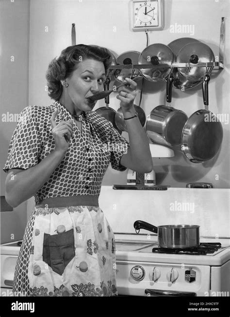 Woman In Her Mid 30 S In An Apron Standing In Front Of Her Stove While