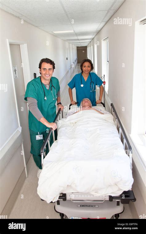 Male And Female Doctor Moving Patient On Bed Along Hospital Corridor