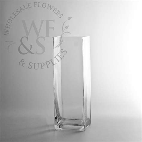 A Tall Glass Vase Sitting On Top Of A White Table Next To A Logo For Wholesale Flowers And Supplies