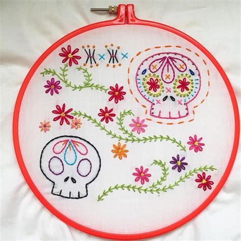 A Close Up Of A Embroidery On A White Surface With Flowers And A Skull