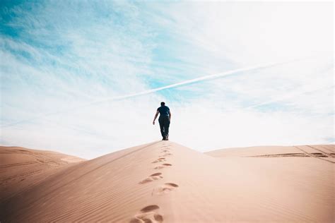 A Person Walking In The Desert Leaving Footprints With Cloud In The