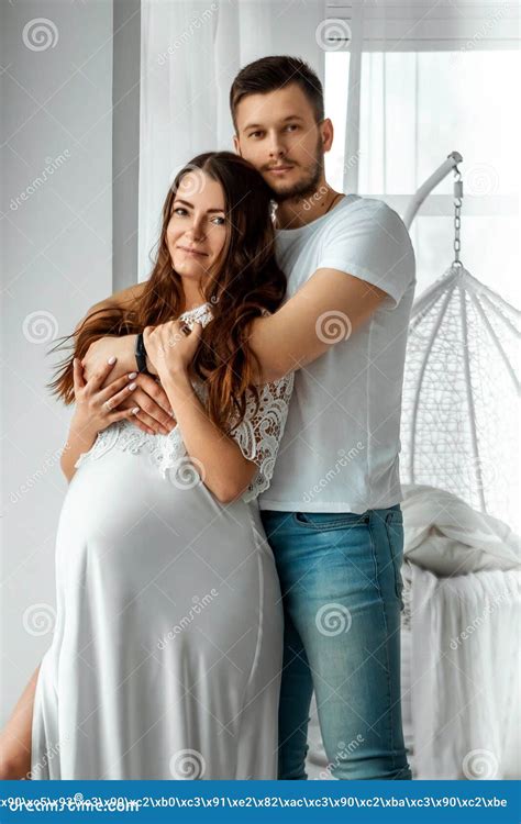 A Pregnant Girl With Her Husband Are Standing In A Bright Bedroom