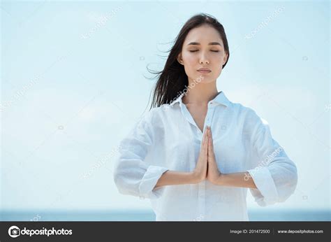 Download Concentrated Asian Woman With Closed Eyes Doing Namaste Mudra Gesture In Front Of Sea