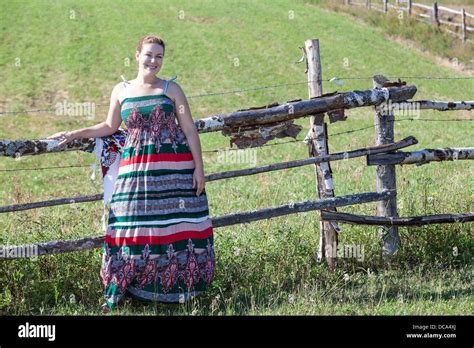 Countrywoman In Sundress Standing Near Village Fence In Field