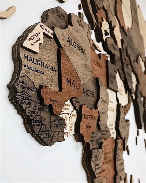A Wooden Cutout Map Of The World On A White Wall With Words Written In