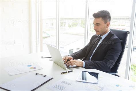 Handsome Businessman Working At Desk With Laptop And Paper Graph In