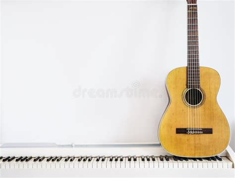 Acoustic Guitar On Piano Keyboard In Front Of White Wall Stock Photo