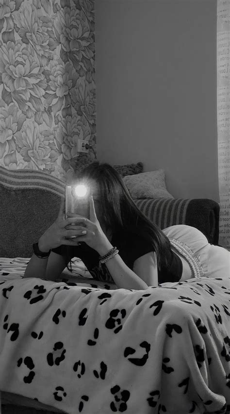 a woman laying on top of a bed under a blanket holding a light up to her face