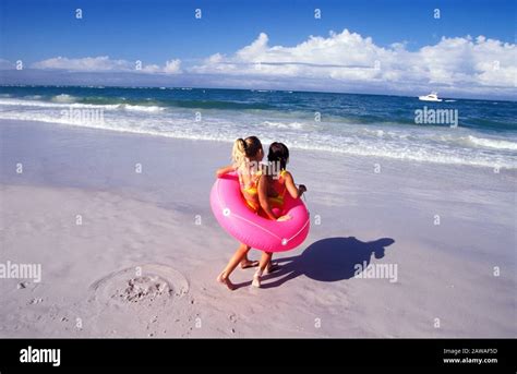 Two Girls Playing With An Inner Tube On The Beach On Summer Vacation
