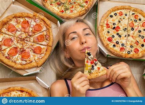 A Young Girl With Blond Hair In A Pink Tank Top Is Holding A Slice Of