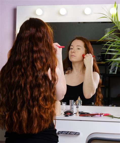 Young Woman With Long Red Hair Preens In Front Of A Mirror Stock Photo