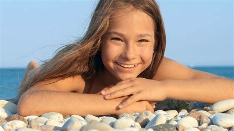 Young girl smiling on sea beach. Portrait of smiling girl lying on pebble beach at summer ...