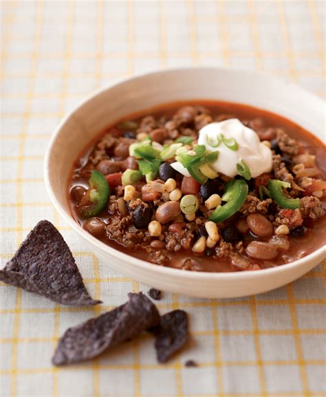 A White Bowl Filled With Chili And Beans Next To Tortilla Chips On A