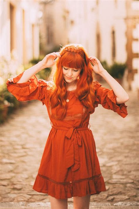A Woman With Red Hair Is Standing In The Street Wearing An Orange Dress And Holding Her Hands