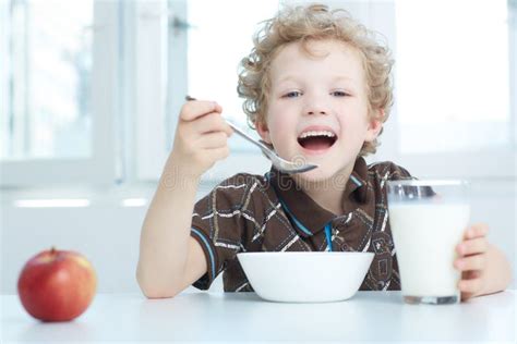 Happy Smiling Boy Eating Cereal While Having Breakfast In The Kitchen