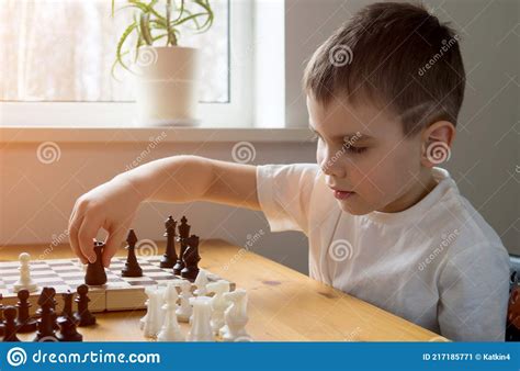 A Preschool Boy Arranges Pieces On A Chessboard For Playing Chess