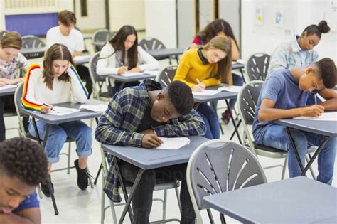 Focused High School Students Taking Exam At Desks In Classroom Stock Photo