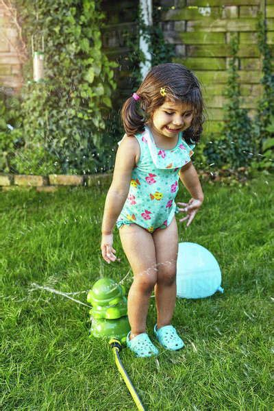 Babe Girl Playing In Garden Beside Water Sprinklers Stock Photo