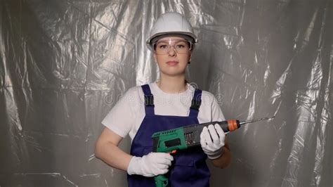 Woman Builder In Blue Overalls And White Hard Hat Helmet With Puncher