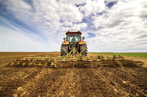 Back View Of Farmer In Tractor Plowing Field In Spring Stock Photo