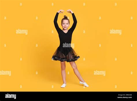 Cute Little Girl In Black Dress Dancing On Yellow Background Stock