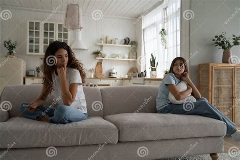 Upset Quarreled Woman And Girl Sit On Opposite Sides Of Sofa In Living Room Look Back At Each