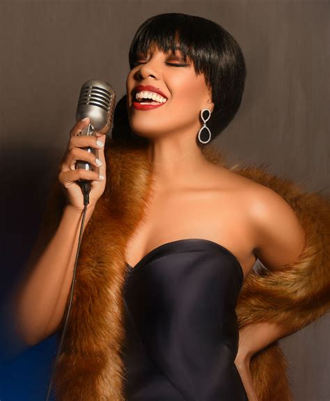 A Woman In A Black Dress Holding A Microphone And Wearing A Fur Stole Around Her Neck