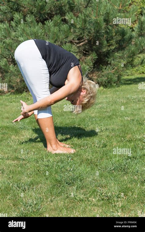 Side View Of Flexible Senior Woman Is Forward Bending Outdoors Stock