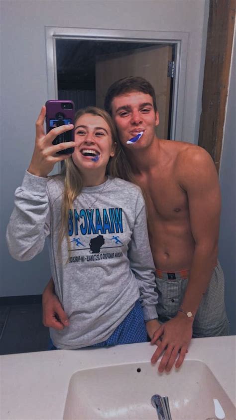 A Man And Woman Brushing Their Teeth In Front Of A Bathroom Mirror While Taking A Selfie