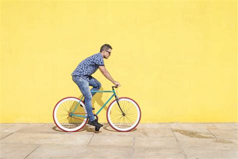 Side View Of Man Riding Bicycle Against Yellow Wall At Sidewalk In City