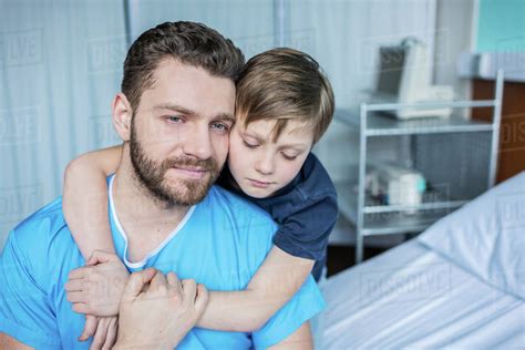 Father And Son Hugging While Sitting On Hospital Bed Dad