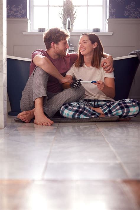 excited couple with woman with prosthetic arm sitting on bathroom floor with positive pregnancy