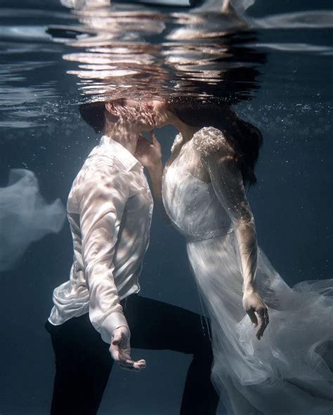 A Man And Woman Kissing Under The Water In Their Wedding Gowns While Holding Each Other S Hands