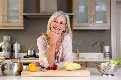 Older Attractive Woman Leaning On Kitchen Counter With Fresh Produce