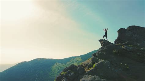 A Man Standing On Top Of A Mountain With And Raising His Hands Up The
