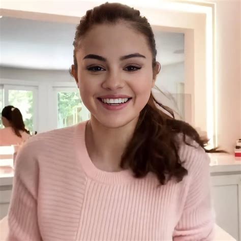 A Woman In A Pink Sweater Is Smiling At The Camera And She Has Her Hair Pulled Back