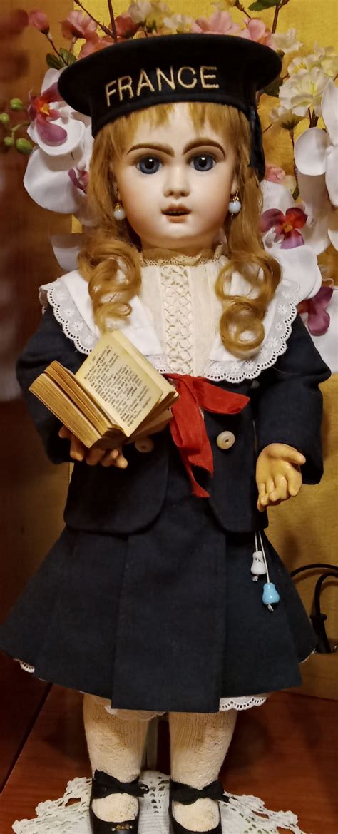 A Doll With Blonde Hair Wearing A Black Hat And Holding A Book In Her Hands