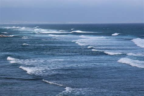 Waves Of The Pacific Ocean Rolling In While Surfers Paddle Out At