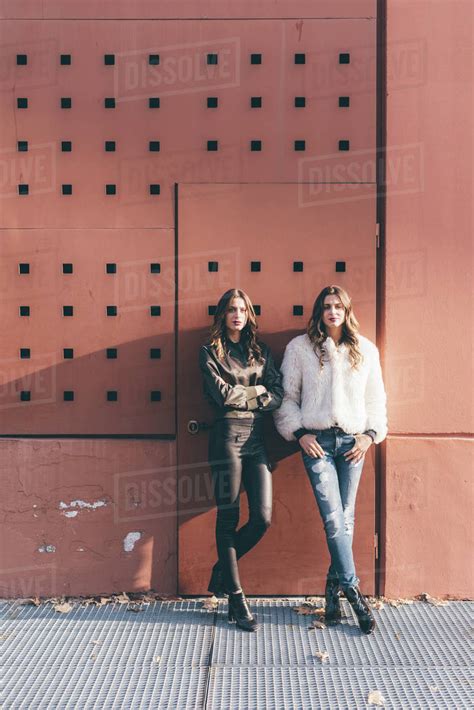 Portrait Of Twin Sisters Outdoors Leaning Against Wall Stock Photo