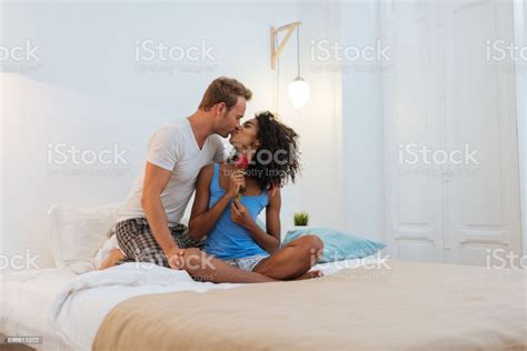 Young Beautiful Interracial Couple In Bed Giving A Surprise Rose Stock