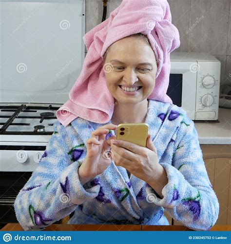 woman in bath towel on her head and wearing bathrobe speaking by phone in kitchen at home
