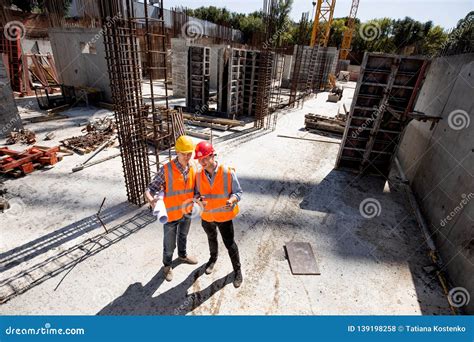Civil Engineer And Architect Dressed In Orange Work Vests And Hard Bats