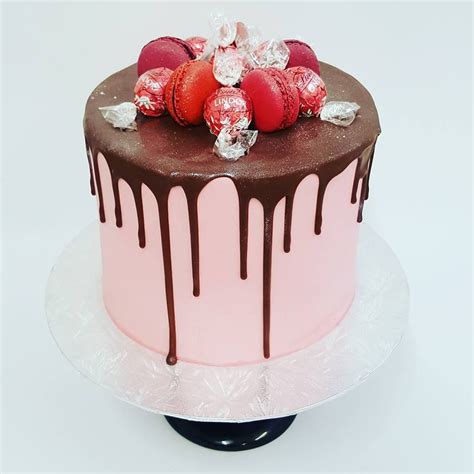smooth light pink drip cake with macarons and lindt balls postres